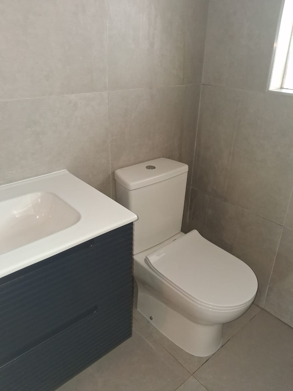 Fully finished grey-tile bathroom with navy vanity and white toilet by Ndumanyani Plumbing